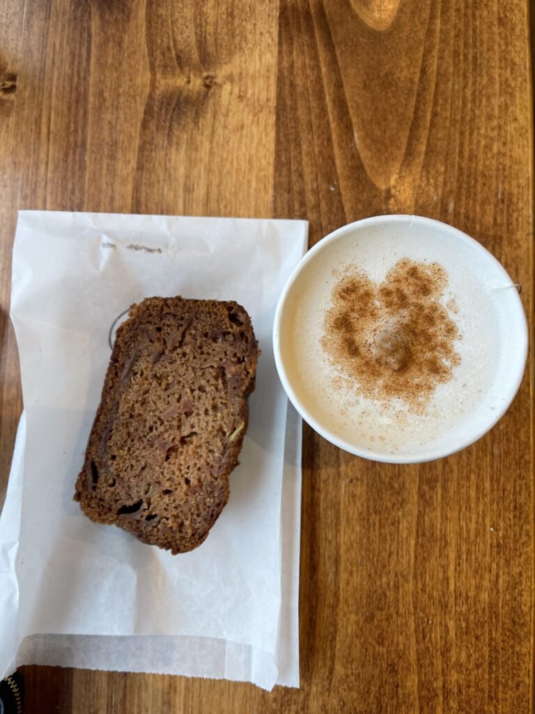 Birds eye view of a slice of apple cake and an autumn fog latte with cinnamon on top of a wooden table.