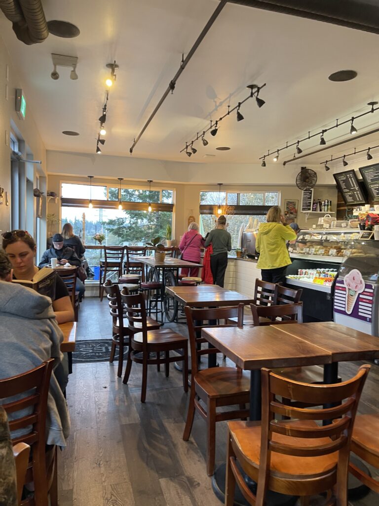 !st person POV of the cafe, with  bunch of wooden tables and chairs and on the right is the cash till.