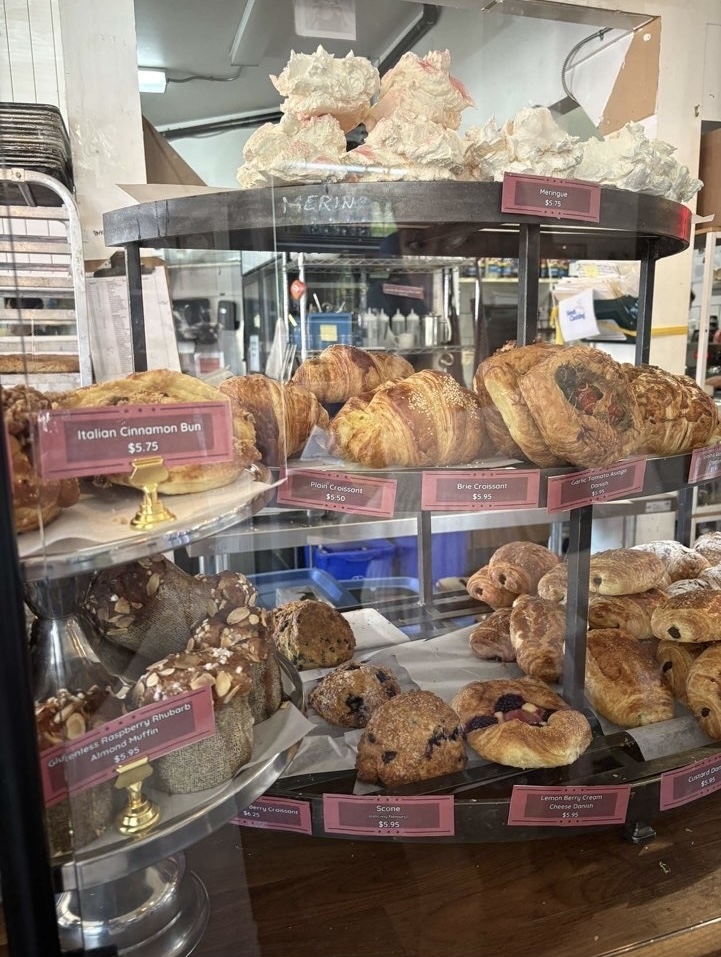 A 3 layer wooden display tray of many bakery items with pink labels.