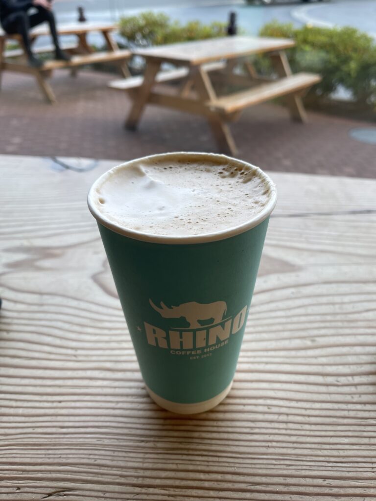 Angled birds eye image of a turquoise coffee cup with the logo of Rhinos with a rhino on top of the word. Cup is placed on a wooden table.